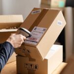 A staff member scans a barcode on a cardboard box, demonstrating barcode price scanning.