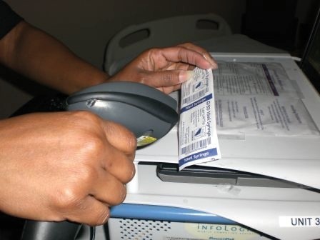 Close-up view of a patient's arm band being scanned with a barcode reader in a hospital setting to verify patient identity.