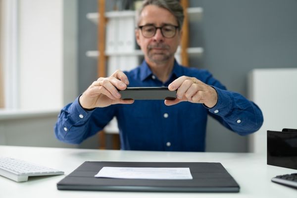 Man using smartphone to scan a signature on paper. This illustrates the step of photographing a signature for digital conversion using a mobile scanning app.